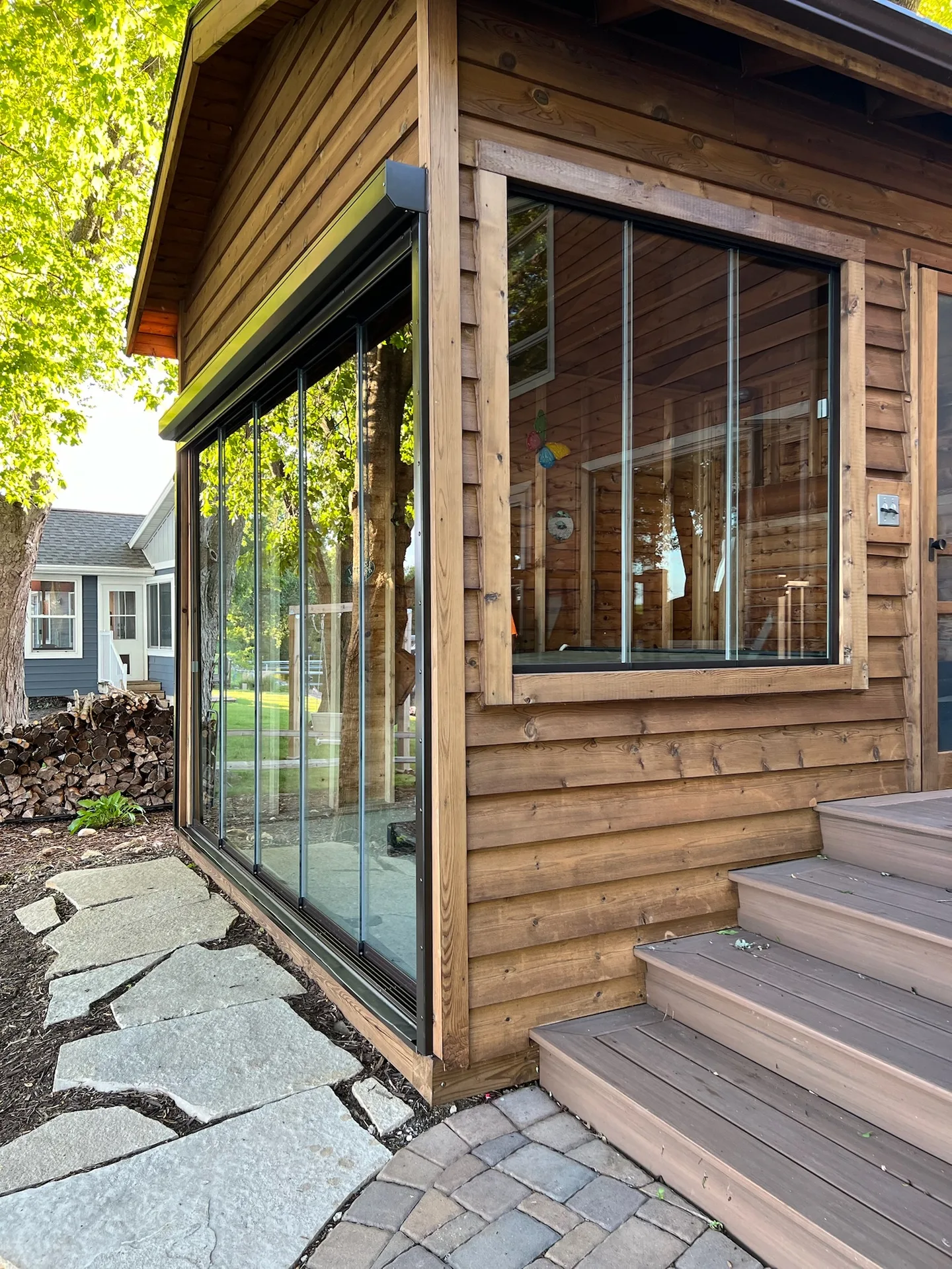 Cedar-sided home with a glass porch enclosure above stone steps
