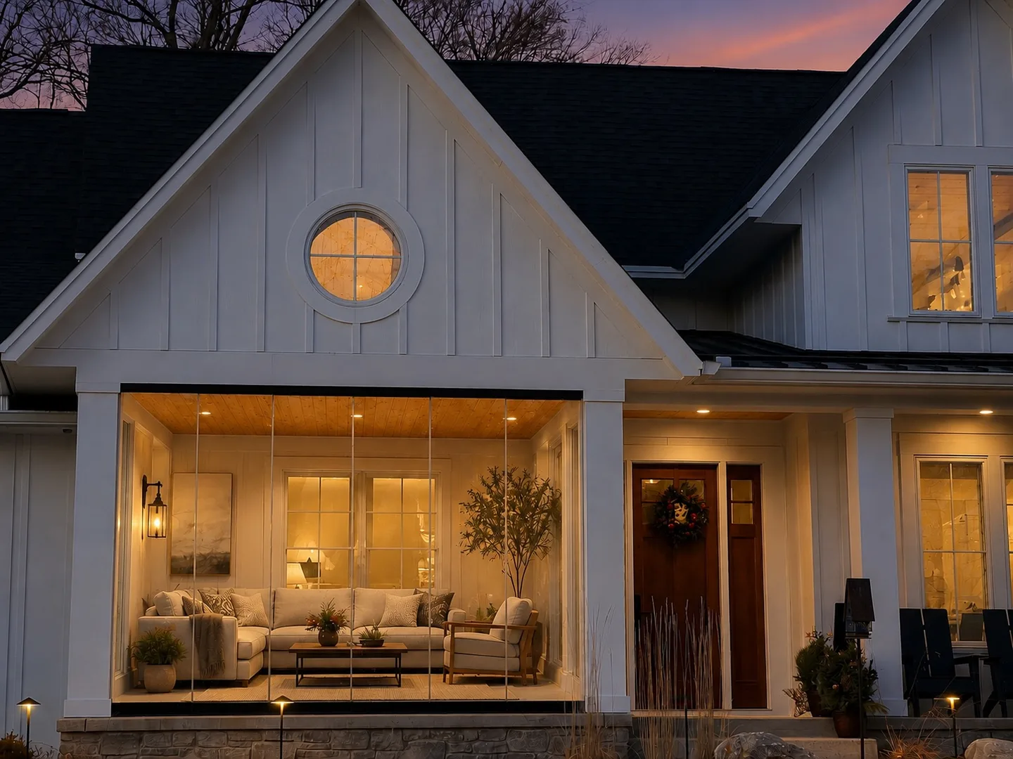 White farmhouse with a round window and a glazed porch glowing at dusk