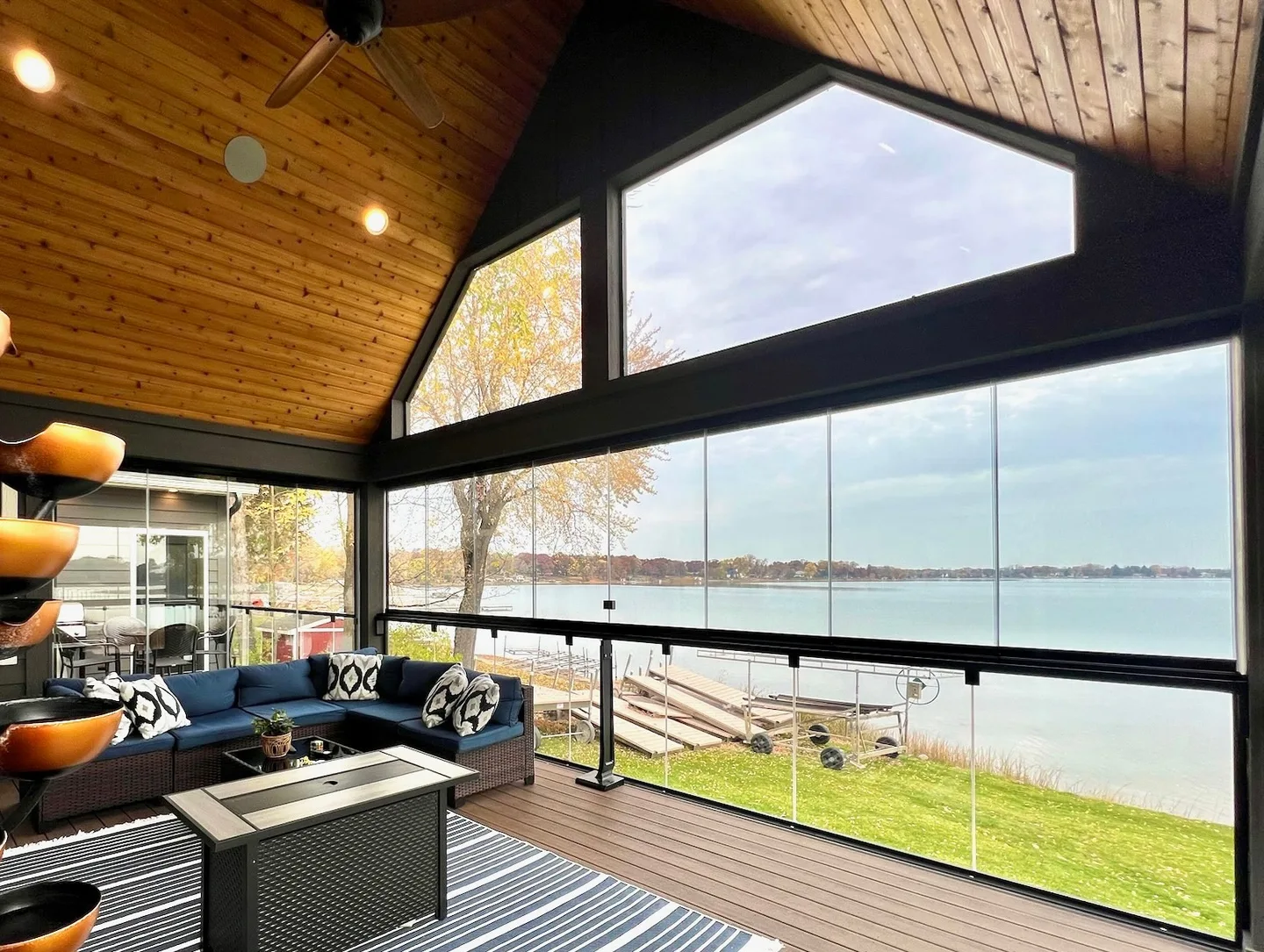 Wood-vaulted porch with a fire table and open water beyond the glass