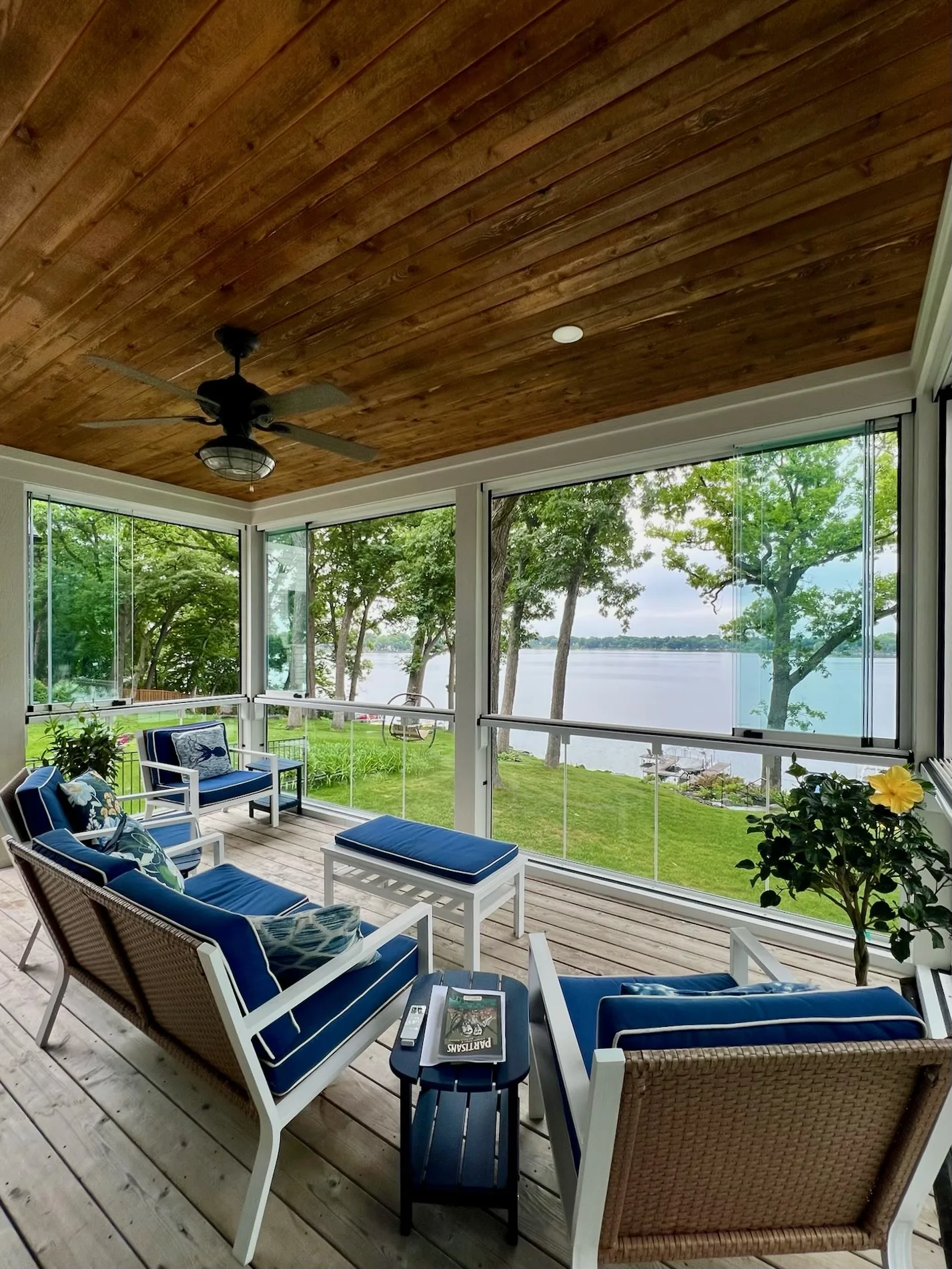Porch with blue seating under a wood ceiling, glass panels facing the lake
